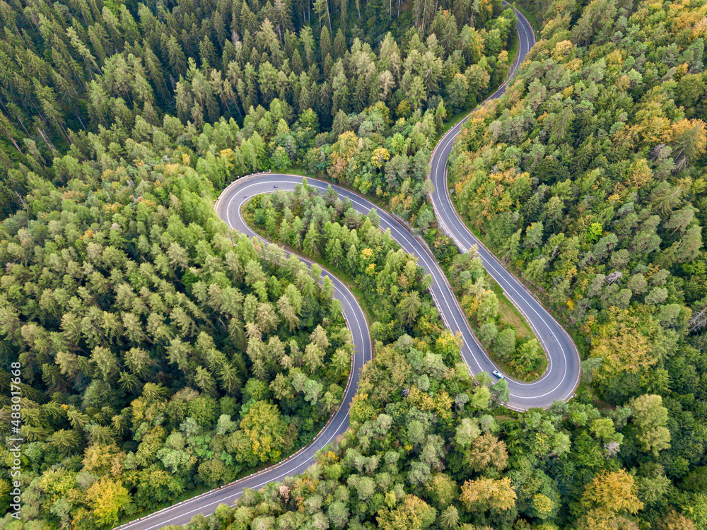 Winding road from high mountain pass, in summer time. Aerial view of a green forest and an empty road traffic 