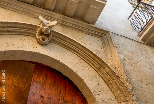 Lecce, Puglia, Italy. August 2021. Detail of a door in the historic center: a stone angel is intent on placing a crown on the arch of the door.