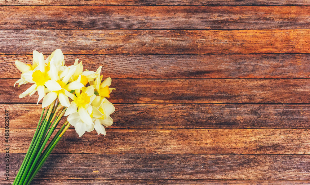 Obraz premium a bouquet of narcissus flowers on a brown wooden background with a copy space