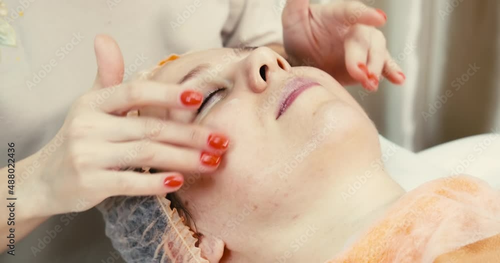 A young beautiful girl lies on a sofa in a beauty salon and receives a facial massage procedure. A young beautiful girl lies on a sofa in a beauty salon and receives a facial massage procedure.