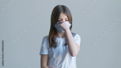 A blonde teenager girl in a white T-shirt stands in a blue mask against a white wall