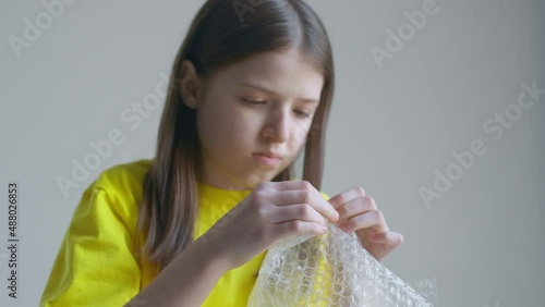 A blonde teenager girl in a yellow T-shirt bursts bubble wrap and is bored