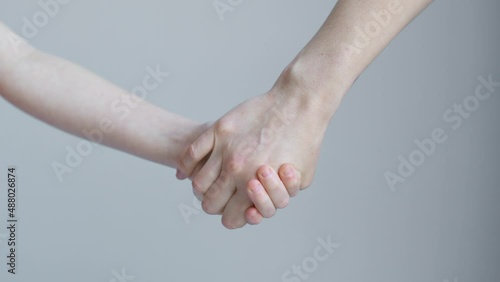 Woman and child join hands and hold in front of the background of a white wall
