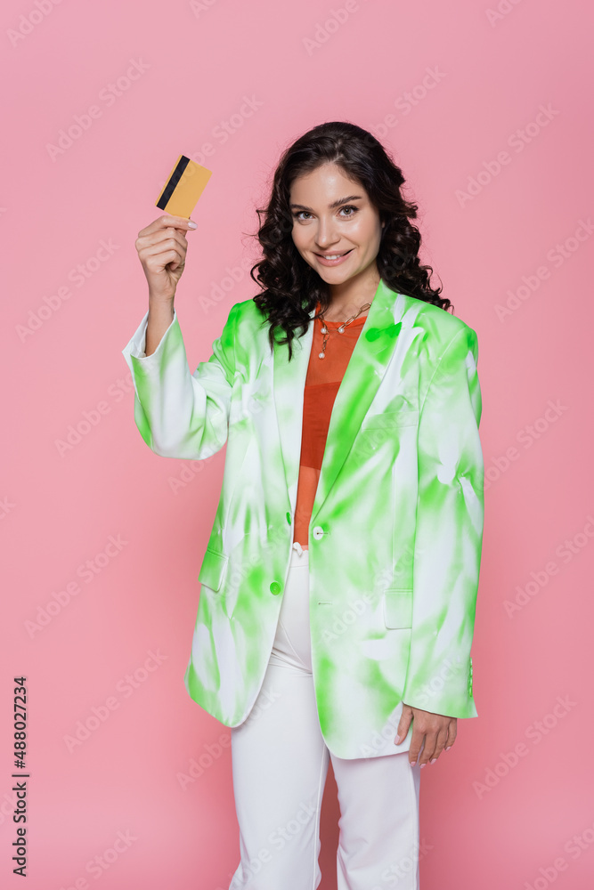 pleased young woman in tie-dye blazer holding credit card isolated on pink. pleased young woman in tie-dye blazer holding credit card isolated on pink.