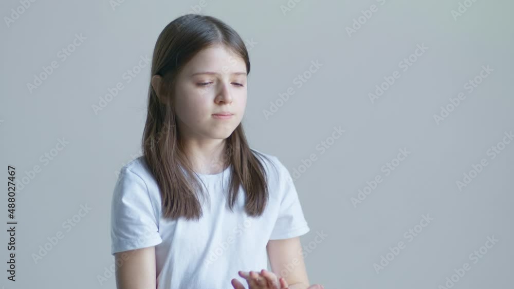 A teenager blonde girl in a white T-shirt and holds a pill in her palm and swallows against the background of a white wall