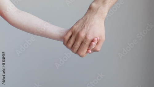 Man and child join hands and hold against the background of a white wall