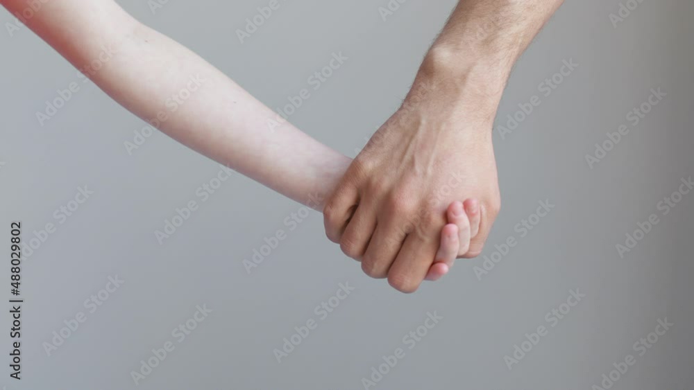 Man and child join hands and hold against the background of a white wall Man and child join hands and hold against the background of a white wall