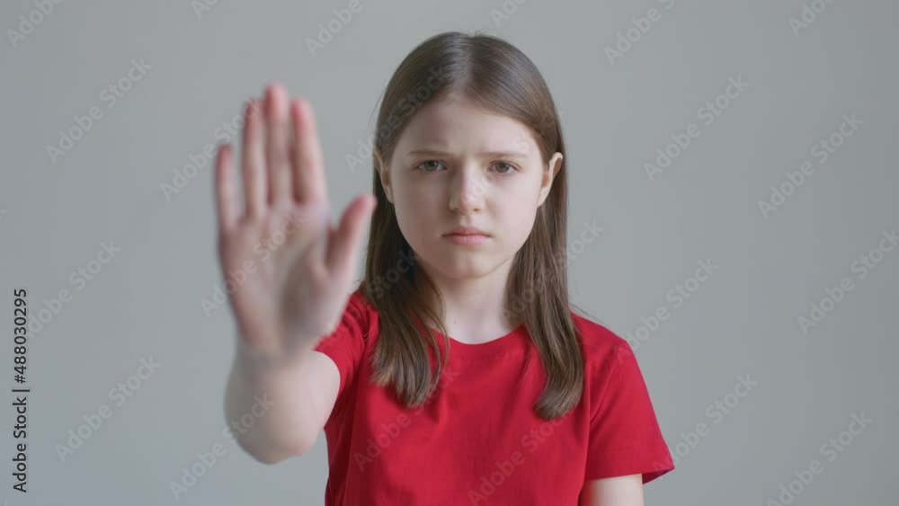 Blonde teenager girl in a red T-shirt angrily raises her hand stop against the background of a white wall Blonde teenager girl in a red T-shirt angrily raises her hand stop against the background of a white wall