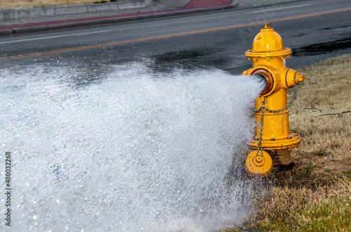 Yellow fire hydrant by four-lane street  gushing water on a winter day