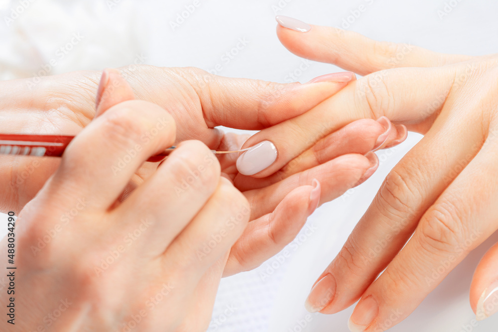 Manicure treatment at nail salon. Manicurist drawing on female nails. Woman in nail salon receiving manicure by beautician. Shallow depth of field Manicure treatment at nail salon. Manicurist drawing on female nails. Woman in nail salon receiving manicure by beautician. Shallow depth of field