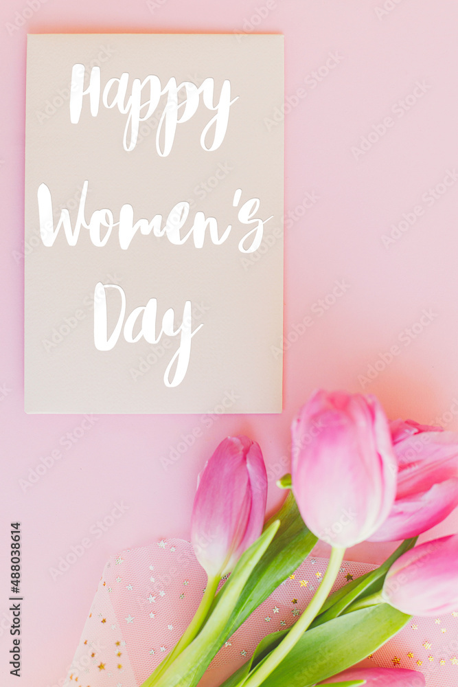 Happy womens day text on pink tulips flat lay on pink background. Stylish greeting card. International Women's Day. 8 march. Handwritten lettering