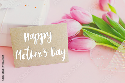 Fototapeta Naklejka Na Ścianę i Meble -  Happy mothers day text on greeting card, pink tulips bouquet and gift box on pink background. Stylish greeting card. Happy Mother's Day, gratitude and love to mom. Handwritten lettering
