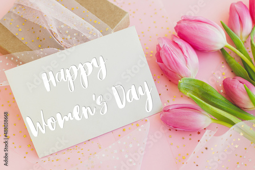 Happy womens day text on greeting card, pink tulips and gift box on pink background. Stylish greeting card. International Women's Day. 8 march. Handwritten lettering