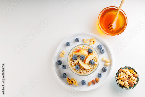 Oatmeal with berries, nuts and honey on a white background. Oatmeal porridge with blueberries and sliced apple in bowl. Healthy breakfast. Top view. Copy space