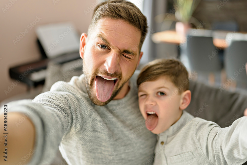 Tableau sur toile Father and son spending time together on sofa taking selfies and making grimaces