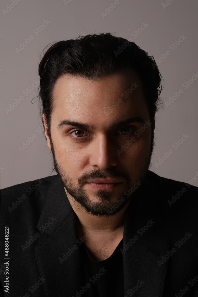Obraz premium Serious bearded man in trendy suit sitting over white wall looking at the camera