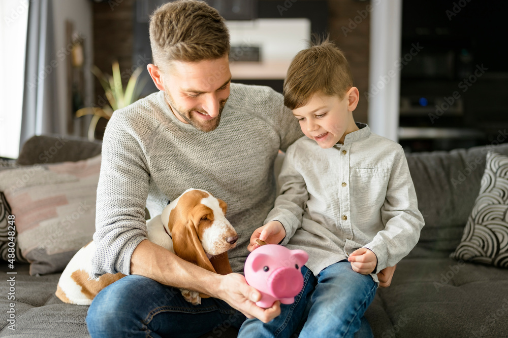 Father or Godfather with Basset dog having fun on the living room At Home puting some money on piggy bank Father or Godfather with Basset dog having fun on the living room At Home puting some money on piggy bank