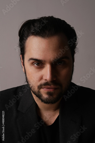 Serious bearded man in trendy suit sitting over white wall looking at the camera