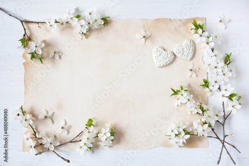 Blossoming branches of cherry plum, hearts and old paper for text on a white wooden background, invitation, greeting card for wedding congratulations.
