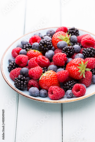 Fresh berry salad on blue dishes. Vintage wooden background.