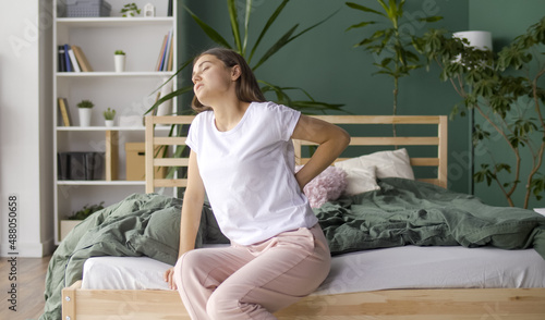 Young Woman Feels Back Pain on the Bed at Home, Rubs Her Lower Back, Trying To Relieve Muscle Tension. Uncomfortable Bed or Mattress, Poor Sleep, Stiffness in Movement, Worsening of Chronic Back Pain.
