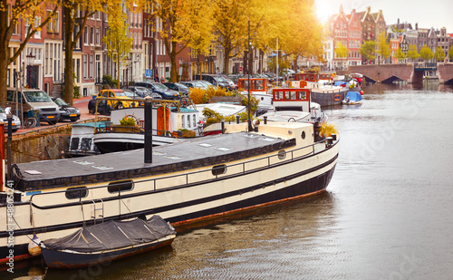 Amsterdam, Netherlands. HouseBoat. Boat house on water of canal along streets with bridge. Autumn landscape with sunset sun. Evening view at the city.