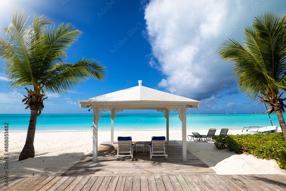 Fototapeta premium A tropical paradise beach with palm trees, a gazebo, sun chairs and turquoise sea without people