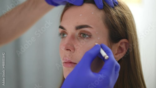 Close-up hand in gloves marking dots for beauty injections on female face. Unrecognizable Caucasian cosmetician preparing client for facelift filler injection. Femininity and beauty care concept photo