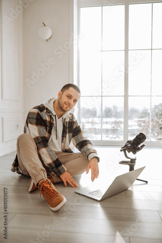 young modern videographer sitting on the floor with equipment with camera, stabilization system steasycam steadicam and laptop. modern european videographer style. guy works editing video on laptop