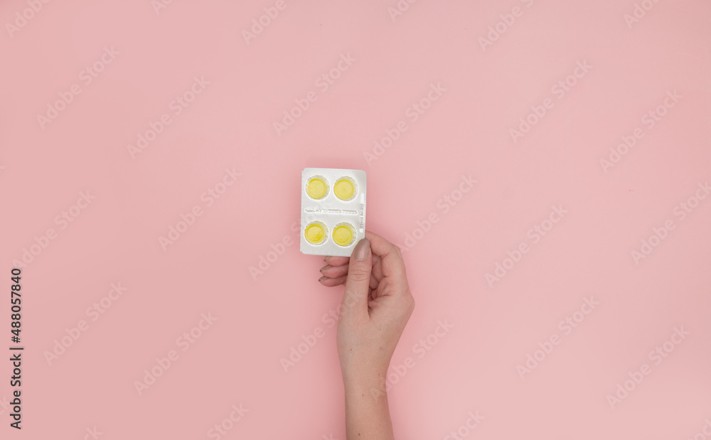 Obraz premium Woman holding blister with cough drops pills tablets on pink background, top view. Space for text