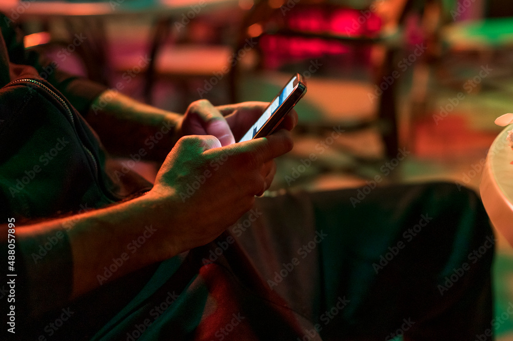 Man texting on the phone in the club sitting on chair.
