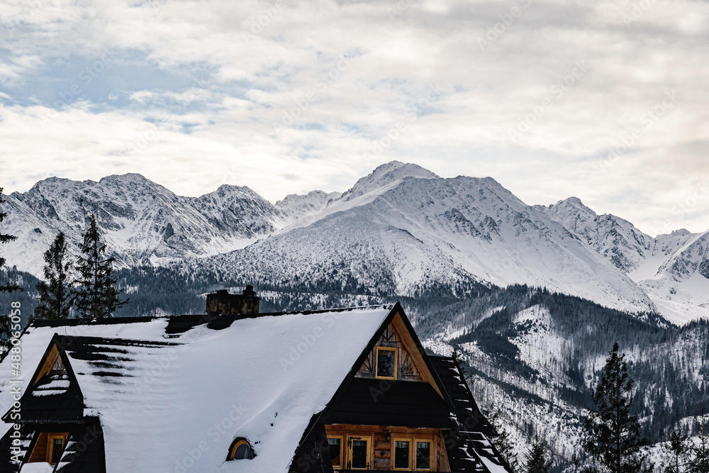 Beautiful view of polish Tatra mountains in winter scenery. In the foreground there is a mountain hut situated among trees, in the background there is a view on the highest peaks of Tatra mountains.
