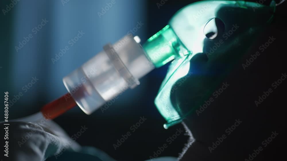 A female patient in medical mask is breathing oxygen support in a hospital next to heart rate machine. Unhealthy woman in coma. Getting mechanical ventilation. Concept of pandemic and therapy. A female patient in medical mask is breathing oxygen support in a hospital next to heart rate machine. Unhealthy woman in coma. Getting mechanical ventilation. Concept of pandemic and therapy.