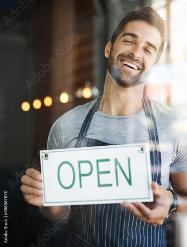 Lets get you some coffee. Shot of a handsome young man hanging up an open sign on the door of his store.