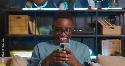 Surfing the web. Happy young African male blogger laughing, smiling using social media with friends online at cozy home. photo