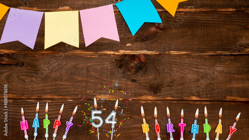 Top view, birthday decorations from letters of candles with fire and festive garlands, save space. Happy birthday background with number 54 on a brown board table. happy birthday to fifty four. photo