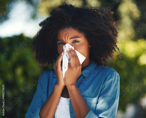 Its allergy season.... Portrait of a young woman blowing her nose with a tissue outside.