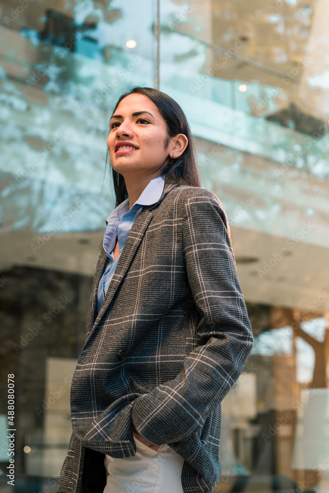 Young entrepreneur woman walking and smiling with the hand in the pocket in front of the office building.