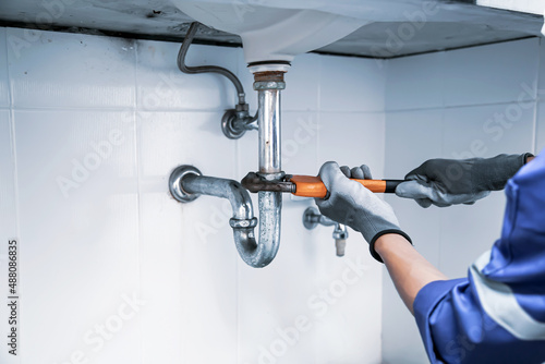 Fotografija Technician plumber using a wrench to repair a water pipe under the sink