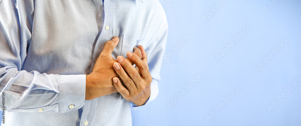 Hand squeezing the left chest pain on blue background concept of heart attack and warning illness heartache angina or heart disease.