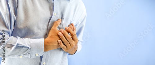 Hand squeezing the left chest pain on blue background concept of heart attack and warning illness heartache angina or heart disease.