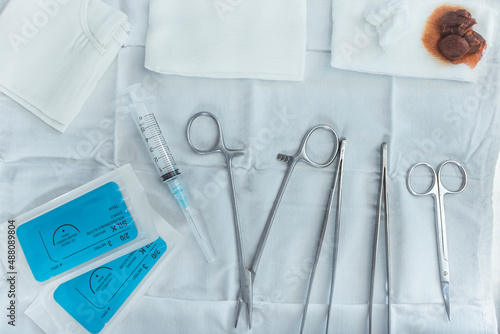 A tray containing medical tools - forceps, toothed forceps, iris scissors,syringe, sutures, iodine soaked cotton, and bandages. Treatment of major laceration or other wounds at the Emergency room. photo