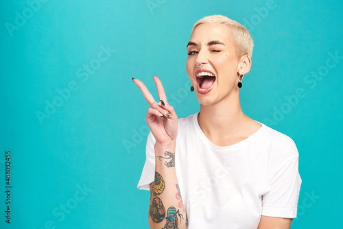 Fill the world with happiness. Studio shot of a confident young woman making a peace gesture against a turquoise background. photo