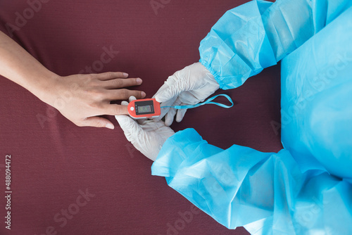 Top view of a nurse in PPE gear inserting an Oximeter on a patient's index finger. Checking blood oxygen or SpO2 levels. At the emergency ward of a hospital. photo