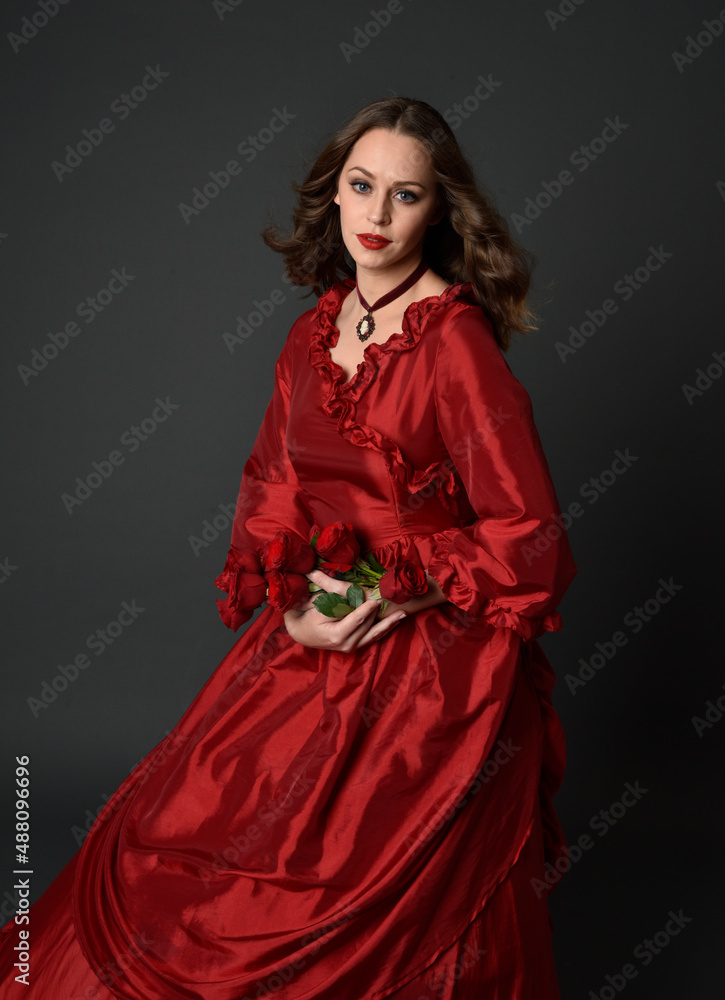 portrait of pretty female model with red hair wearing glamorous historical victorian red ballgown. Posing with a moody dark background. portrait of pretty female model with red hair wearing glamorous historical victorian red ballgown. Posing with a moody dark background.
