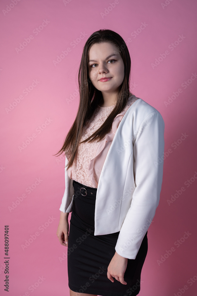 A cute plus-size model stands on a pink background in a white unbuttoned jacket, a pink blouse with lace, a black office skirt and high-heeled shoes. A modest business portrait A cute plus-size model stands on a pink background in a white unbuttoned jacket, a pink blouse with lace, a black office skirt and high-heeled shoes. A modest business portrait