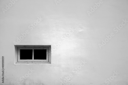 White wall of the house with a small window. The wall of the house is plastered and painted white. Lonely window on the white wall of the building.