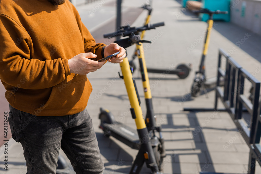 Close-up of male using smartphone after riding by electric scooter in the city. Innovative transport Close-up of male using smartphone after riding by electric scooter in the city. Innovative transport
