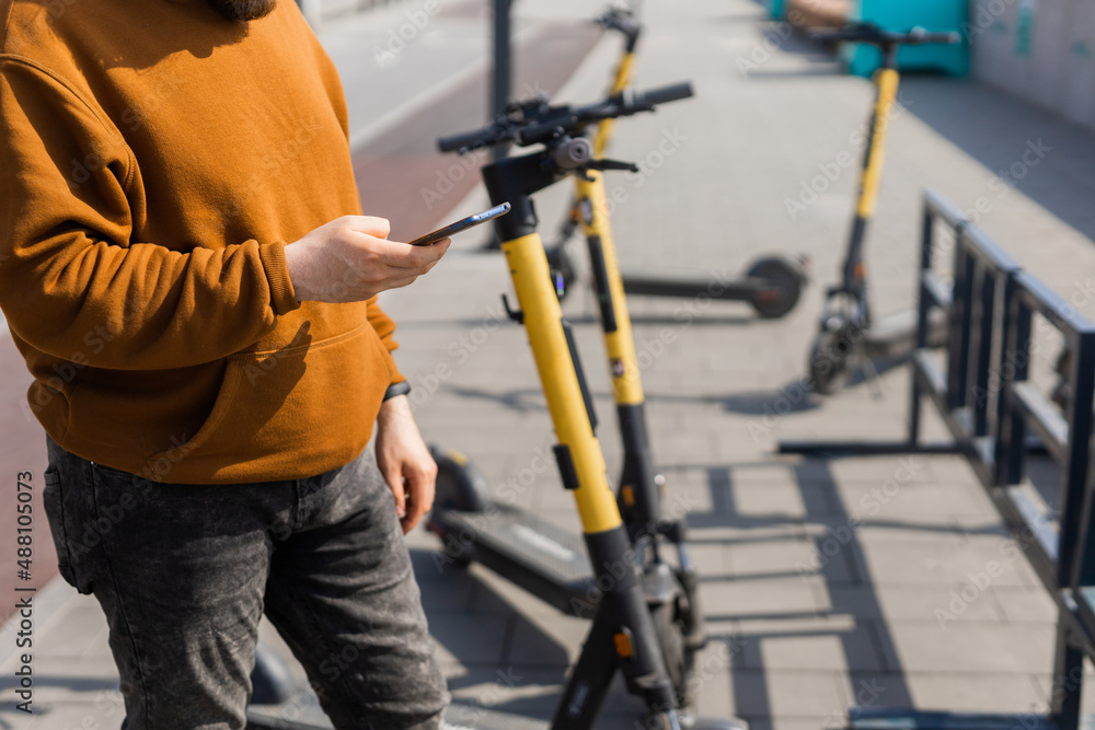 Close up guy is paying for electrical scooter by web payment using his mobile phone. Modern urban transport concept Close up guy is paying for electrical scooter by web payment using his mobile phone. Modern urban transport concept