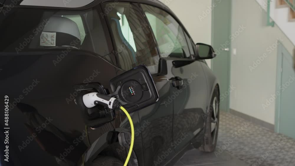 Woman plugs a charger to electric car socket at home after shopping